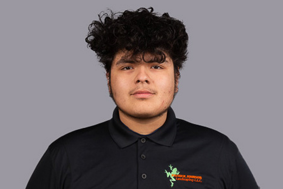 A young man with curly hair is wearing a black polo shirt.