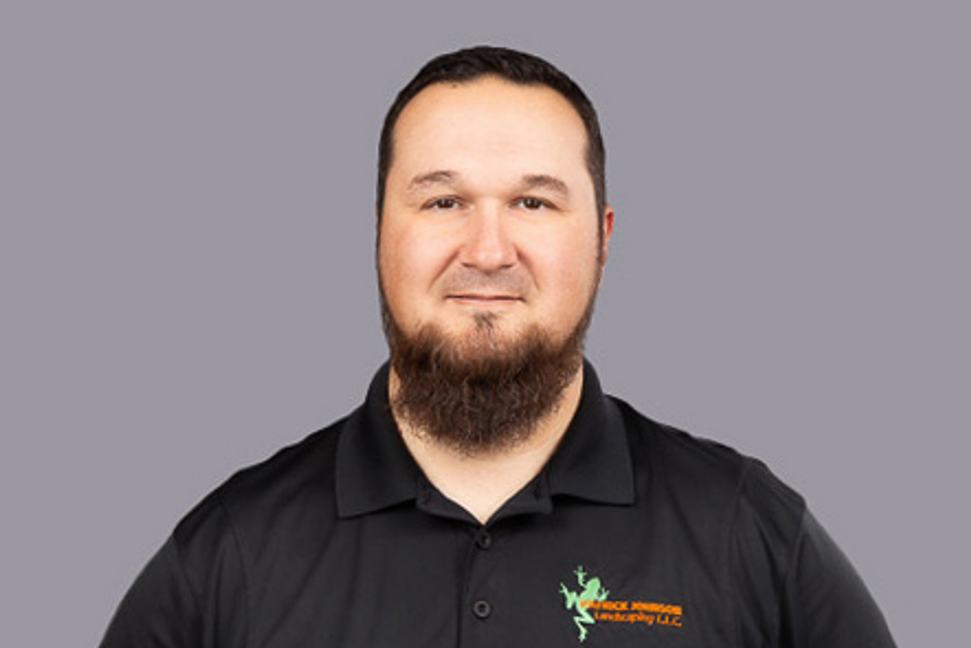 A man with a beard is wearing a black polo shirt.