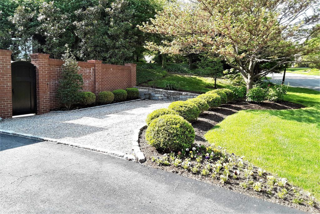 A driveway leading to a house with a brick wall and a gate.