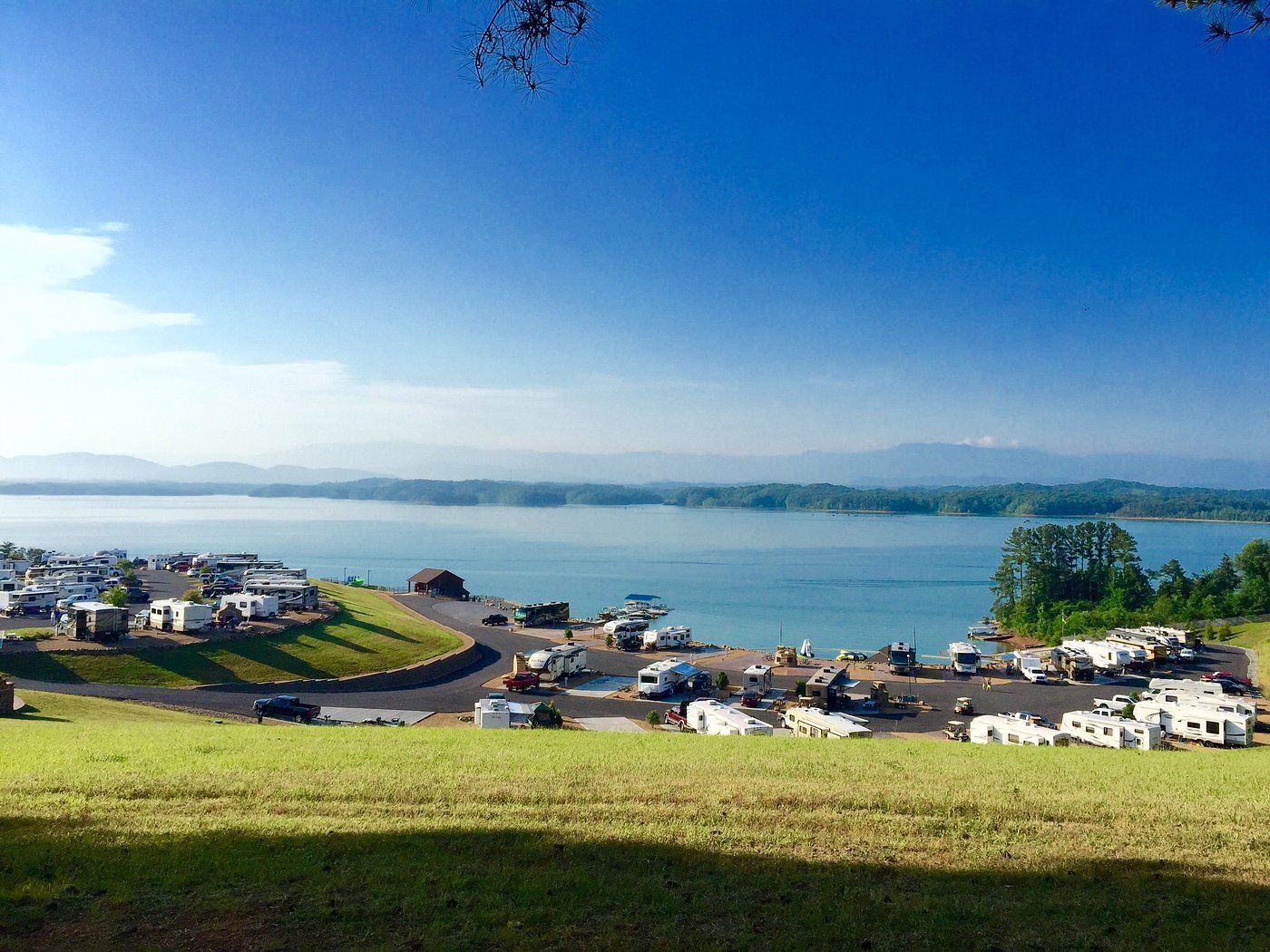 Sunny lakeside harbor with boats, grassy hill, and distant mountains under a clear blue sky in Dandridge, TN. 