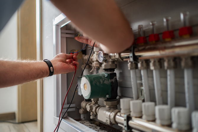 Learn more about our Heating Services Hands adjusting valves on a boiler or heating system inside a utility panel.