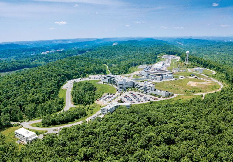 Aerial view of a large industrial complex nestled in green forested hills under a blue sky in Oak Ridge, TN.