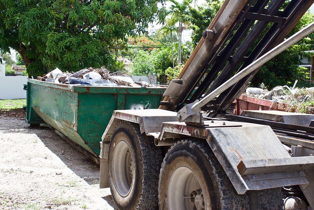 A dump truck is parked by a tree in Miami, FL, representing Grove Tree Service and Landscaping exper