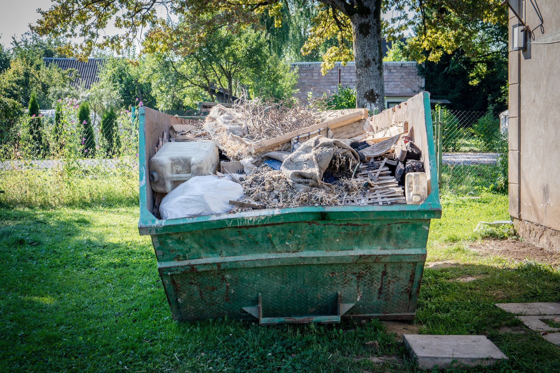 Big green container full of debris, inside an alley and under the sun.