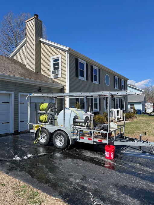 A trailer with pressure washing equipment parked in front of a house on a sunny day.