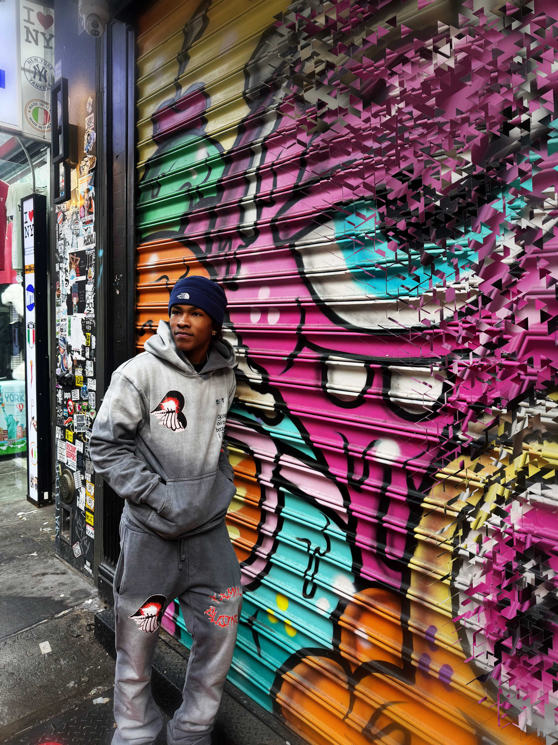 Person in hoodie, beanie, standing by a graffiti-covered storefront shutter.