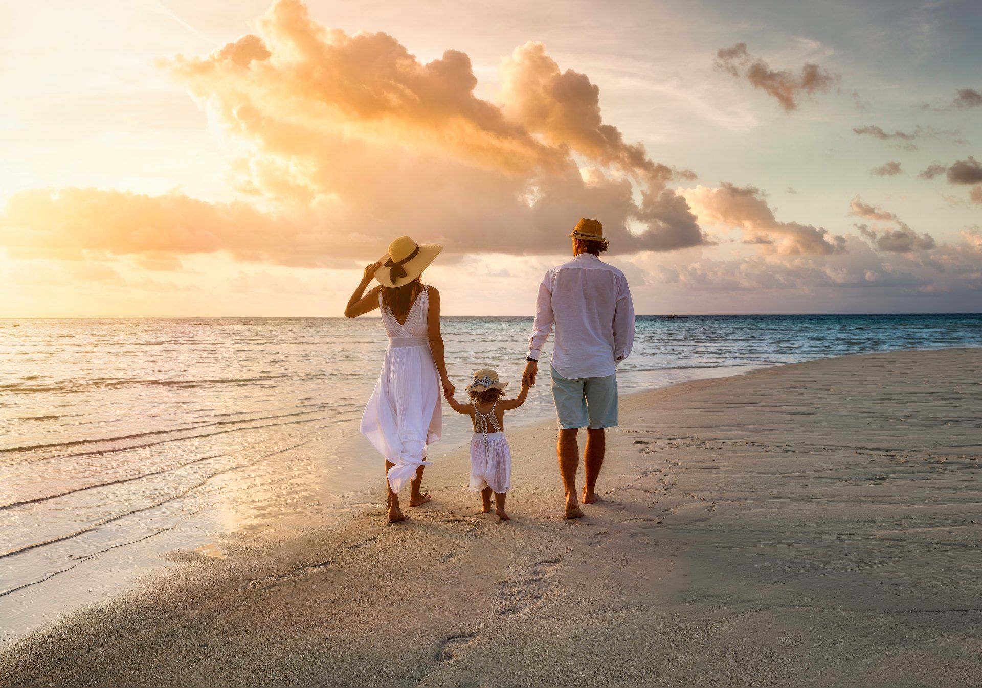 A family is walking on the beach at sunset holding hands.