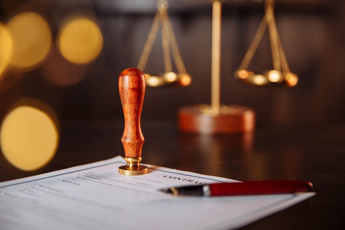 A stamp is sitting on top of a piece of paper next to a pen and scales of justice.