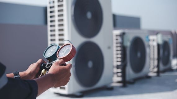 Lake Area Heating and Cooling LLC | A man is holding two gauges in front of a row of air conditioners.