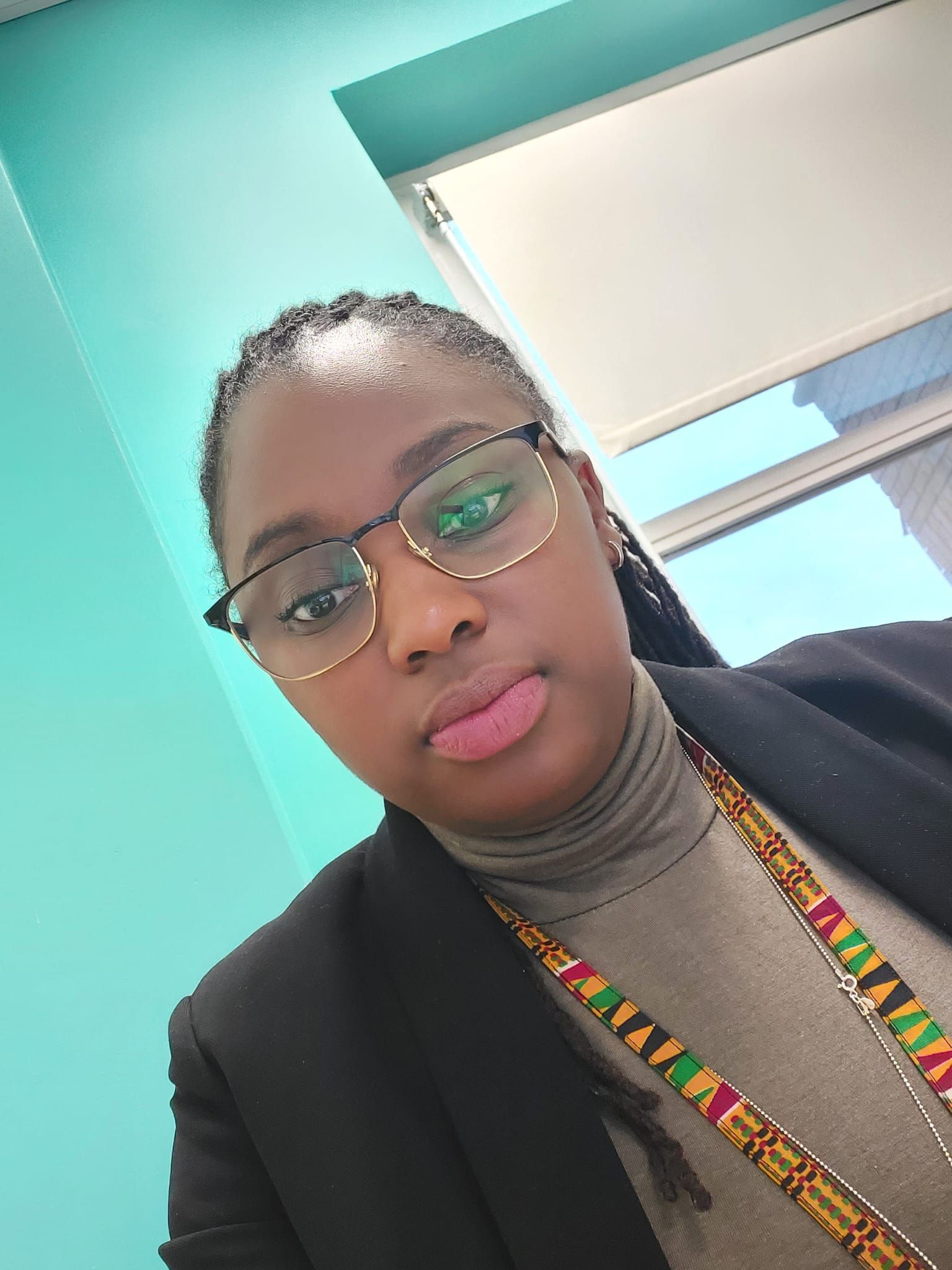 A woman wearing glasses and a necklace is standing in front of a window.