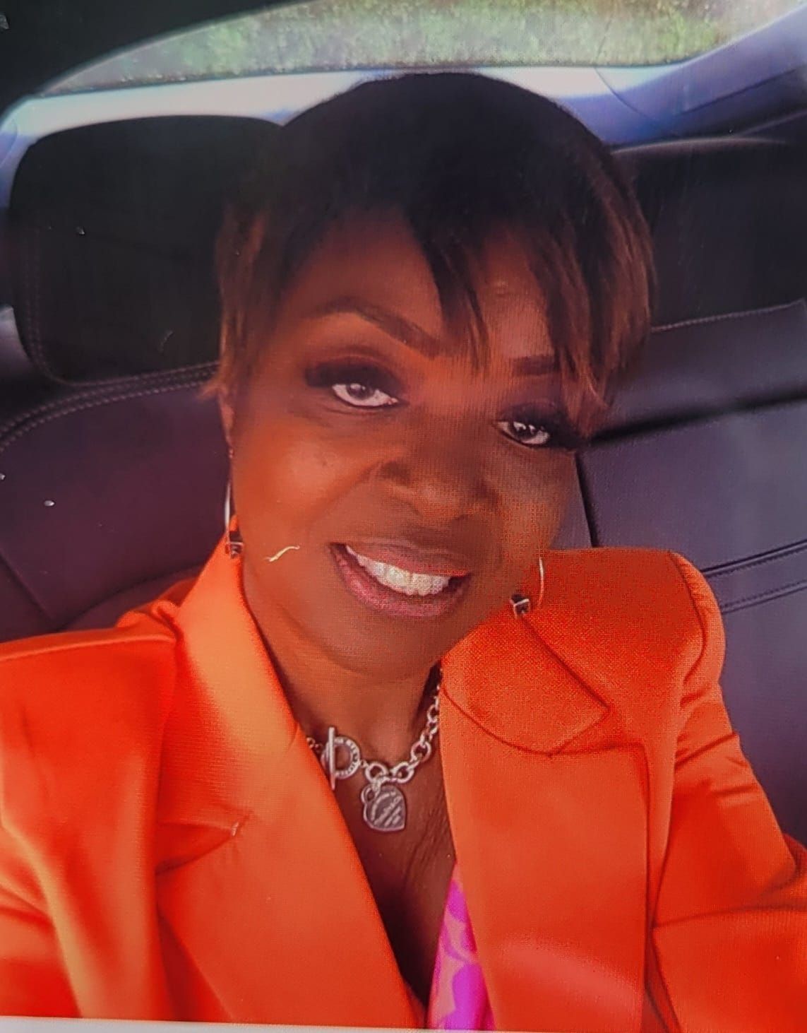 A woman in a car wearing an orange jacket and necklace