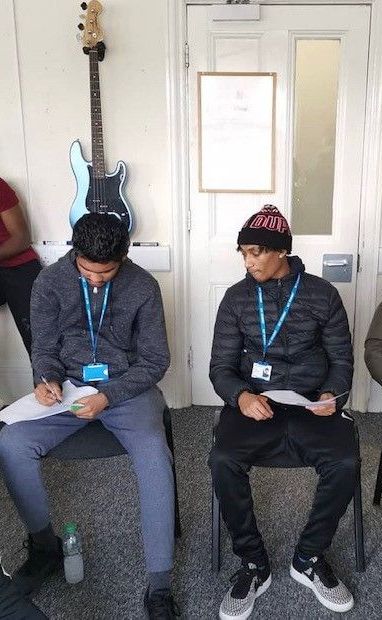Two men are sitting in chairs in front of a guitar.