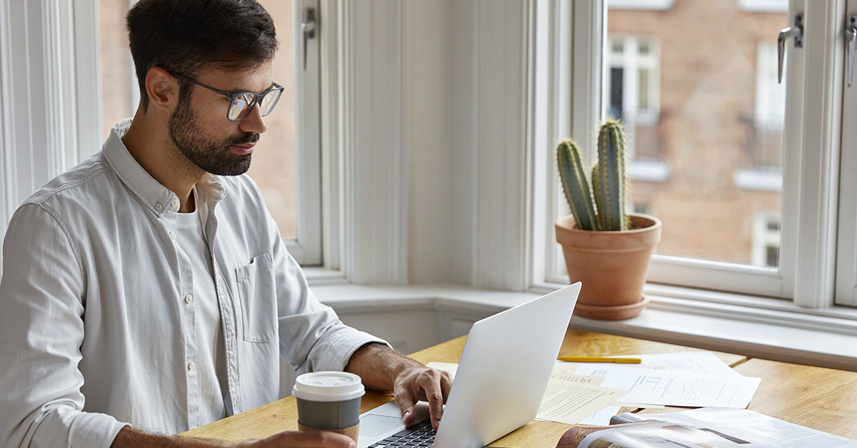 Un hombre está sentado en una mesa usando una computadora portátil.