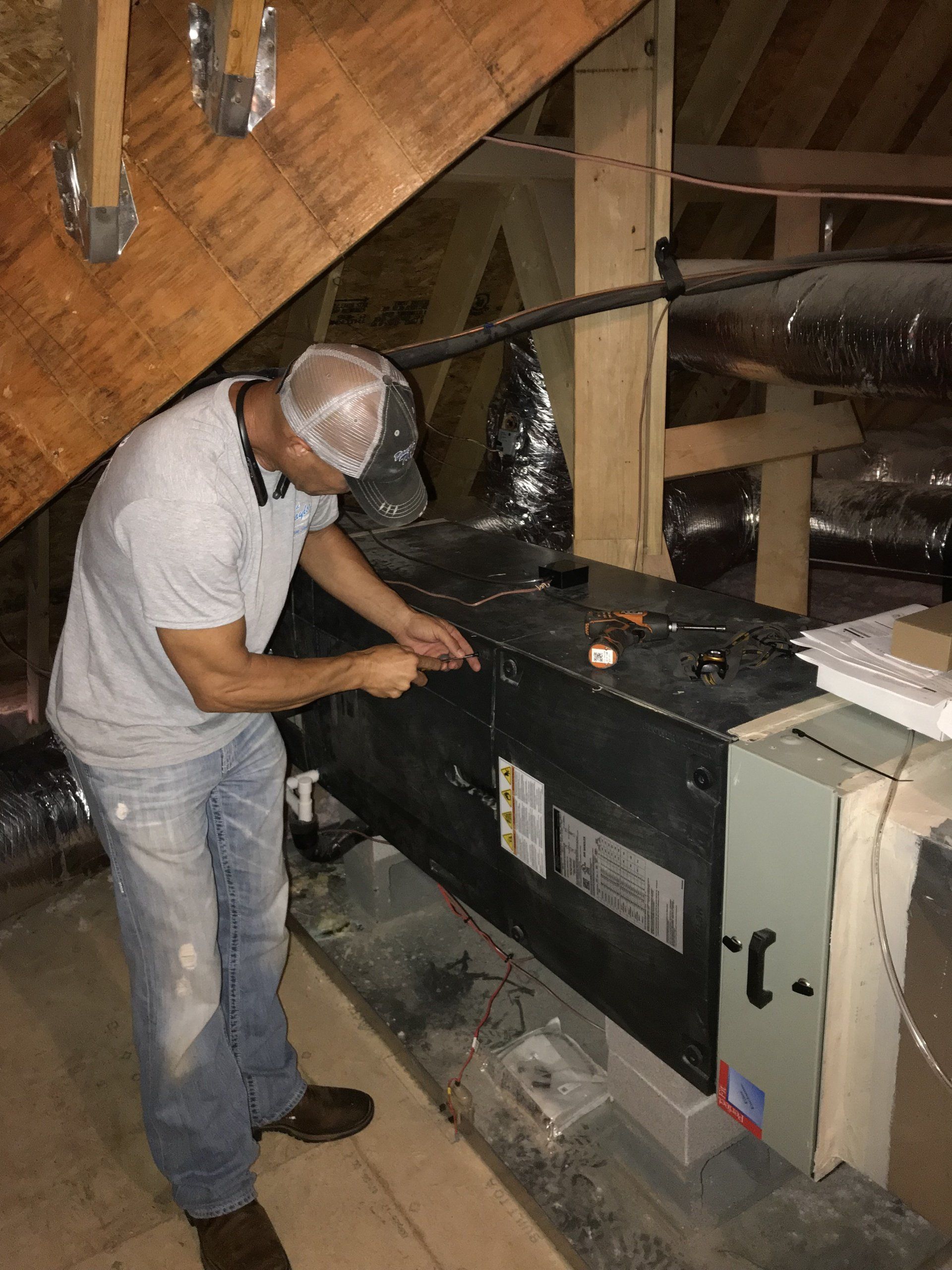 A man is working on an air conditioner in an attic