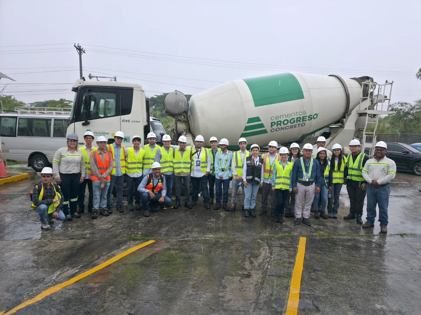 Un grupo de personas con chalecos de seguridad posa frente a un camión hormigonera. Día nublado.