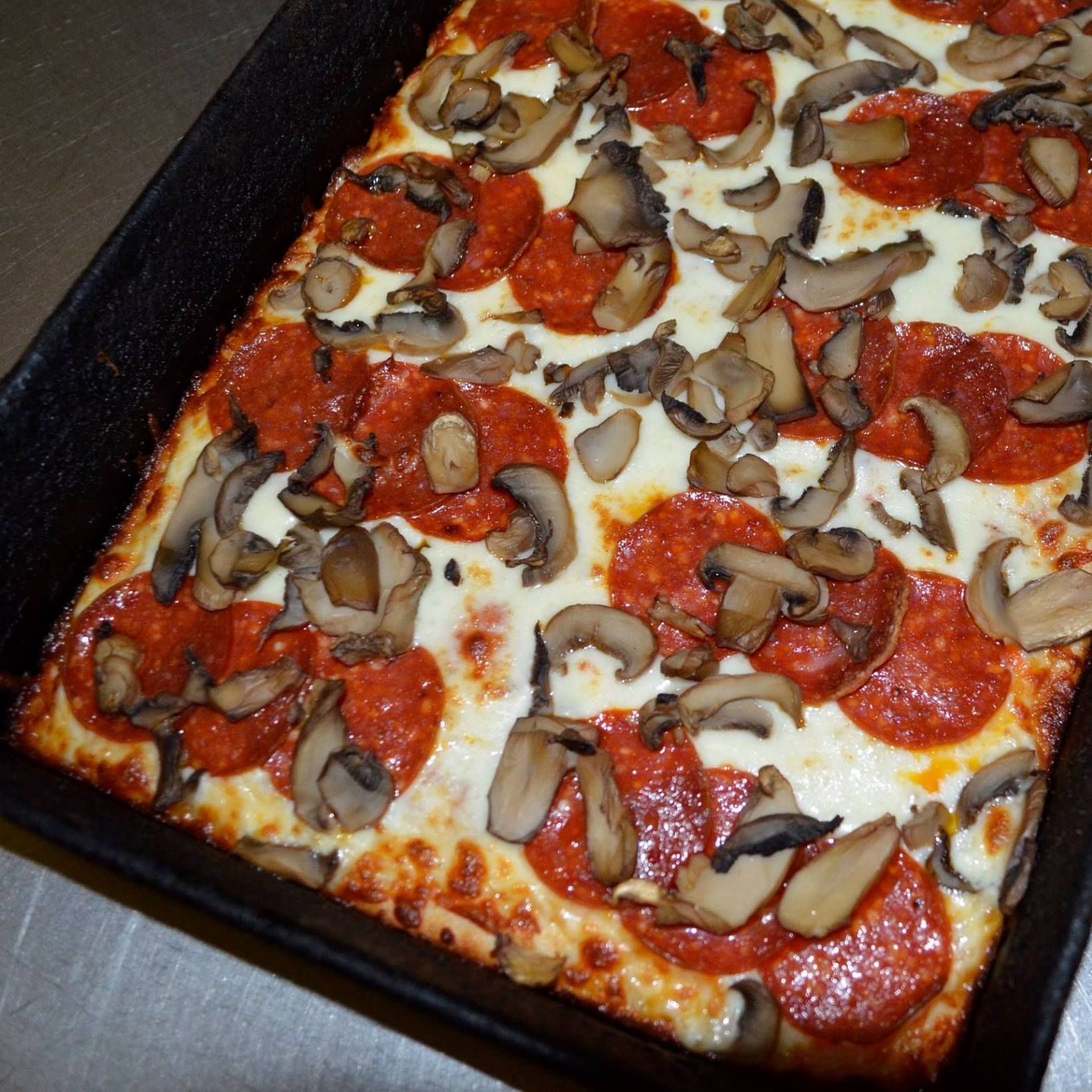 Square pizza with pepperoni and mushrooms in a black baking pan.