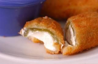 Fried jalapeño poppers with cream cheese filling, on a plate with purple dip.