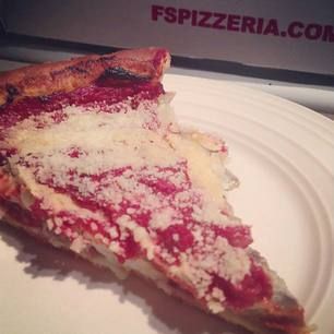 Slice of deep-dish pizza on a white plate, topped with sauce and cheese, near an FS Pizzeria box.