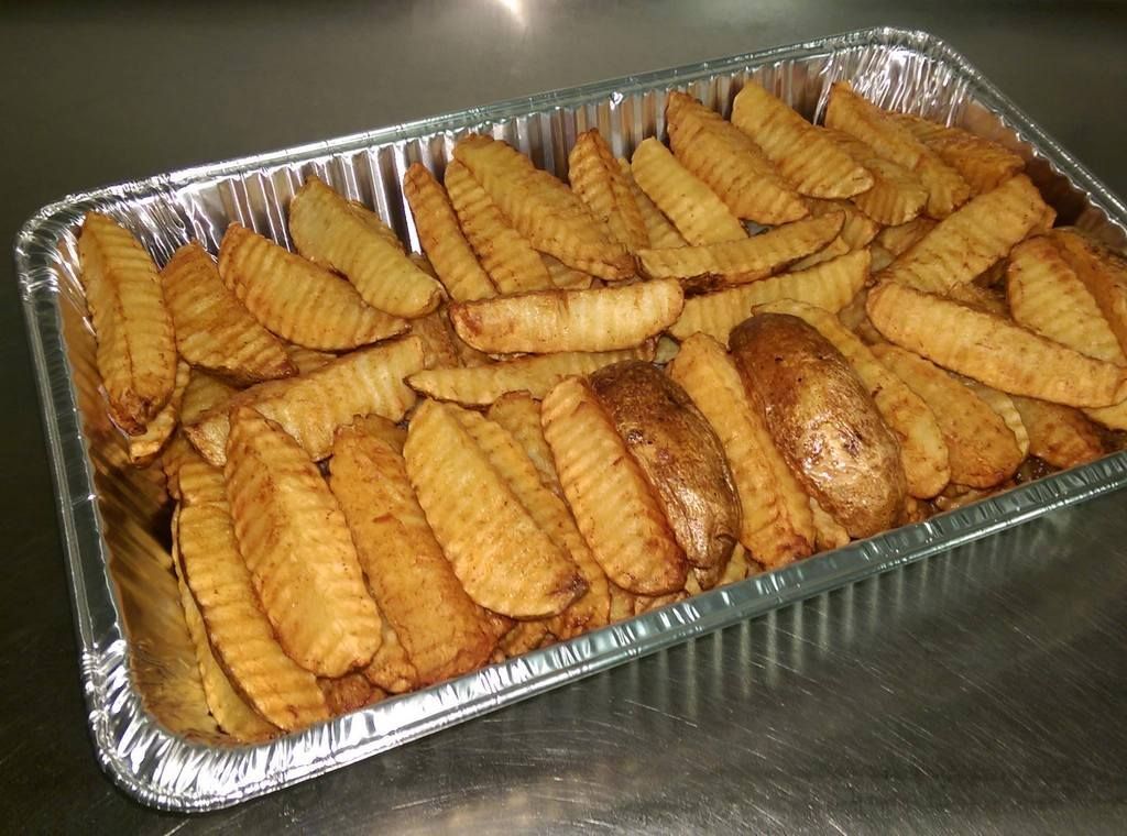Tray of golden, seasoned potato wedges in a foil container on a metal surface.