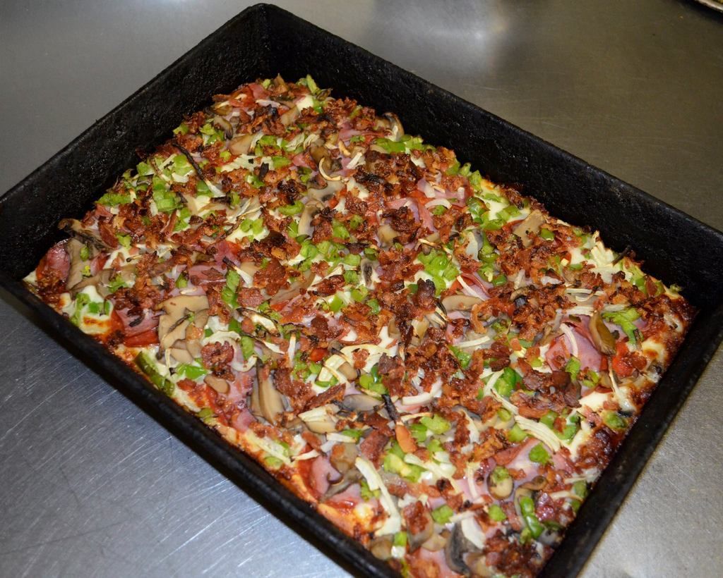 Baked rectangular pizza with assorted toppings in a black pan.