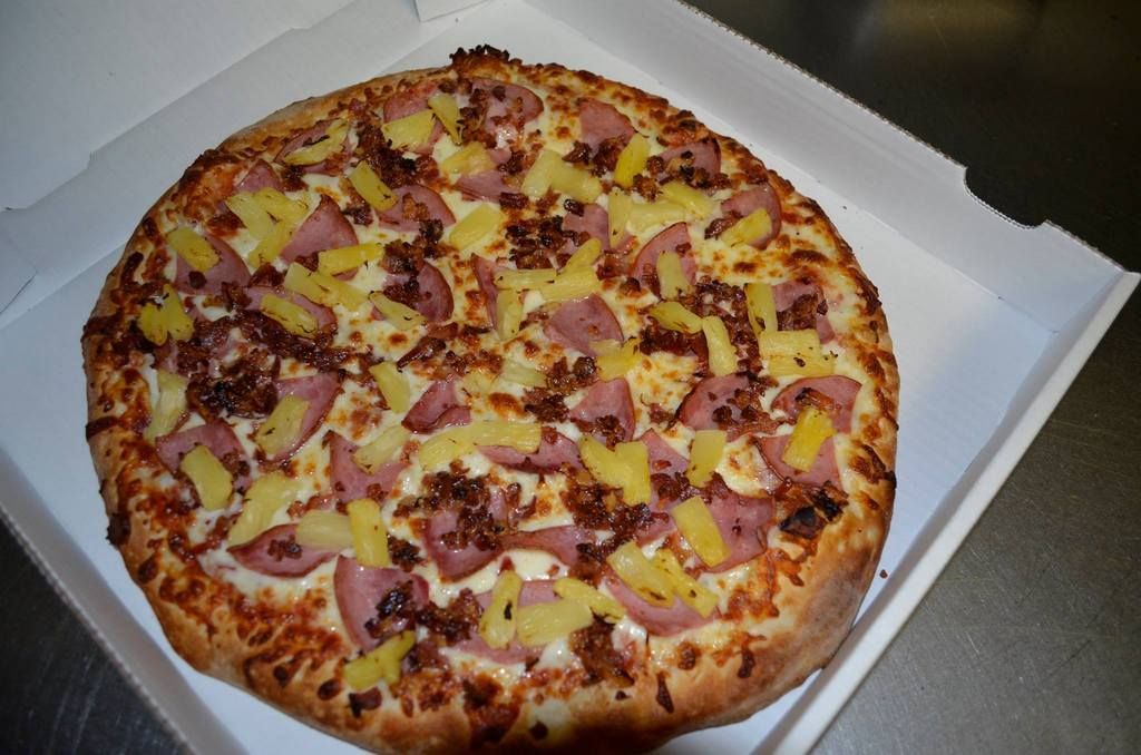 Pizza with pineapple, ham, and bacon in a white cardboard box.