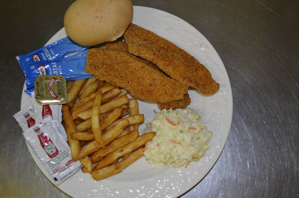Plate with fried fish, fries, coleslaw, bun, and condiments.