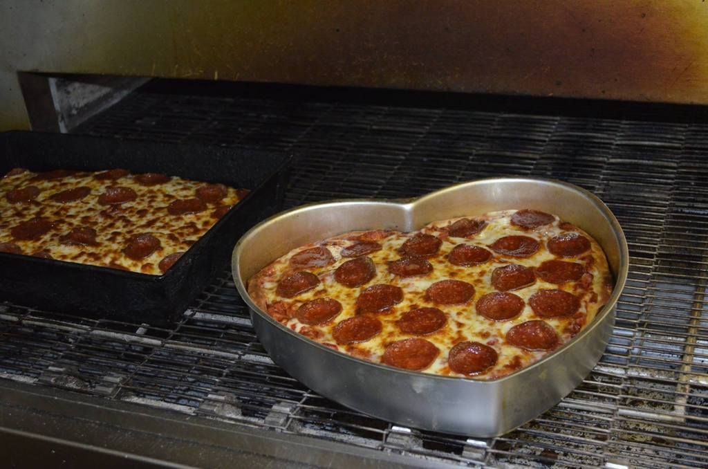 Pizza in heart-shaped pan and rectangular pan in an oven, topped with pepperoni.