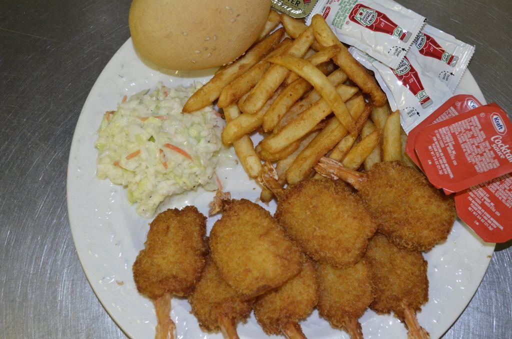 Plate of fried shrimp on skewers, fries, coleslaw, bun, and condiments.