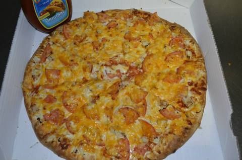 Pizza in a box with sauce bottle. Cheesy, topped with meat, brown crust.