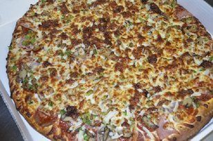 Large, fully-loaded pizza with various toppings including sausage, vegetables, and cheese in a delivery box.