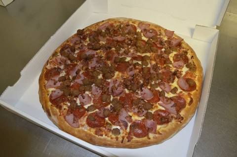 Meat-lovers pizza in a white pizza box, topped with pepperoni, sausage, ham.