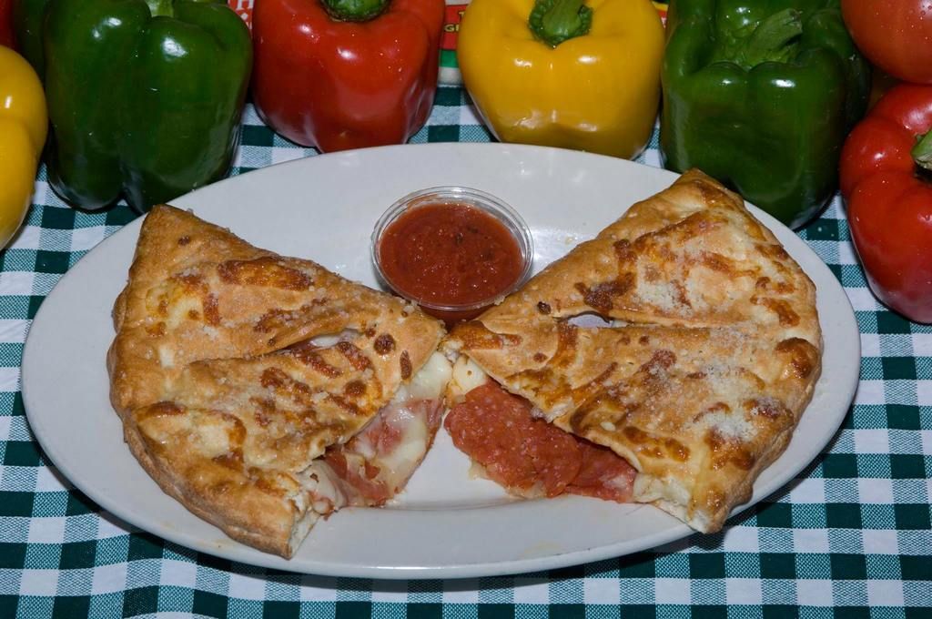 Calzone cut open, revealing pepperoni and cheese, with marinara sauce on a plate, surrounded by bell peppers.