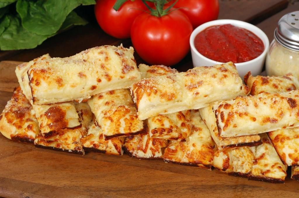 Cheese breadsticks on wooden board with tomatoes, marinara, and parmesan.