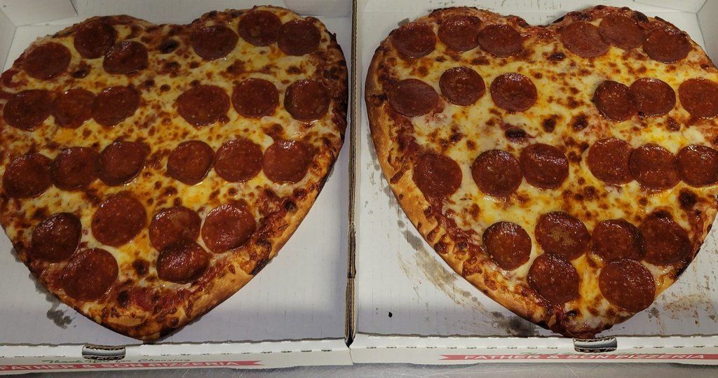 Two heart-shaped pizzas with pepperoni in pizza boxes.
