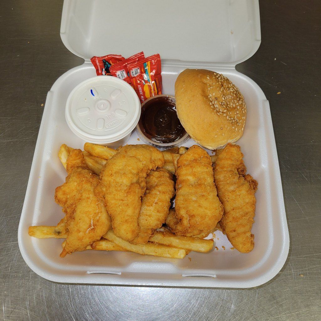 Chicken tenders and fries meal with bun, sauces, and drink in a styrofoam container.