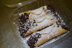 Cannoli pastries dusted with powdered sugar and chocolate chips in a plastic container.
