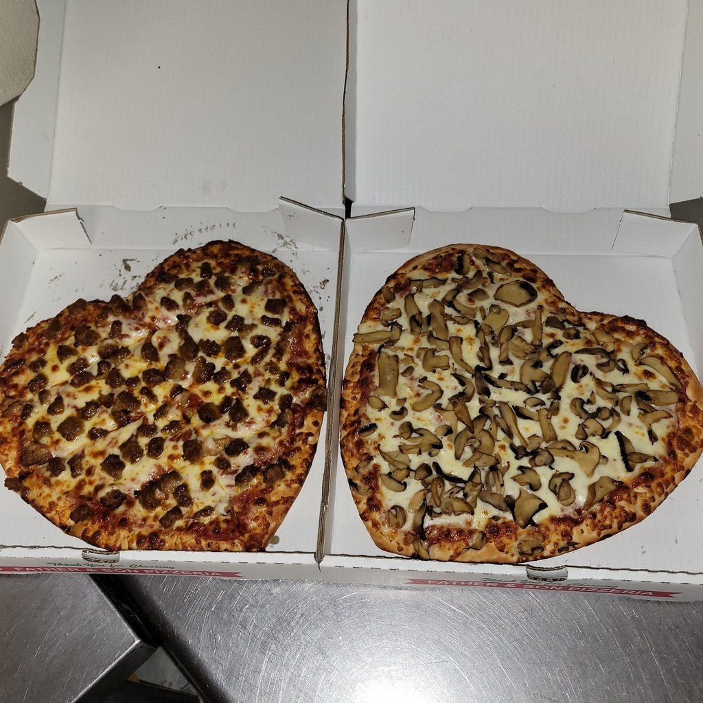 Two heart-shaped pizzas in open pizza boxes, one with sausage, the other with mushrooms.