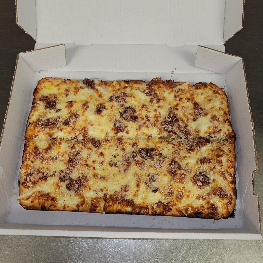 Square pizza in a cardboard box, covered in cheese and visible toppings.