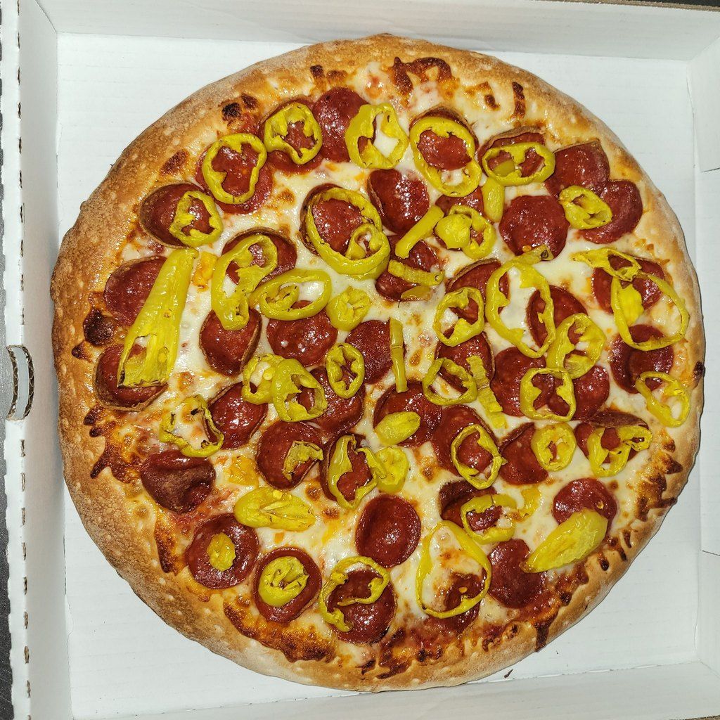 Pepperoni pizza topped with yellow pepper rings in a white box.