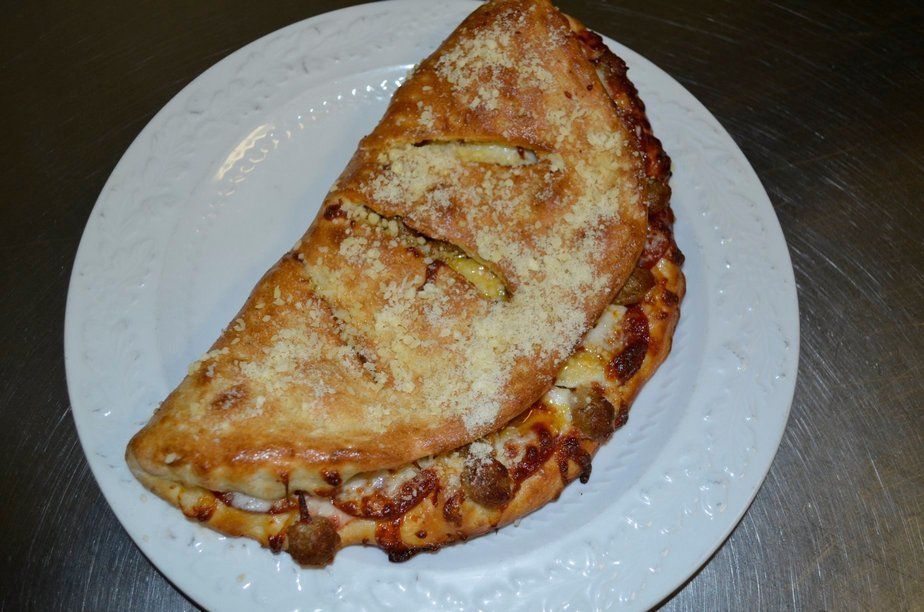 Calzone on a white plate, golden-brown crust, visible filling, sprinkled cheese.