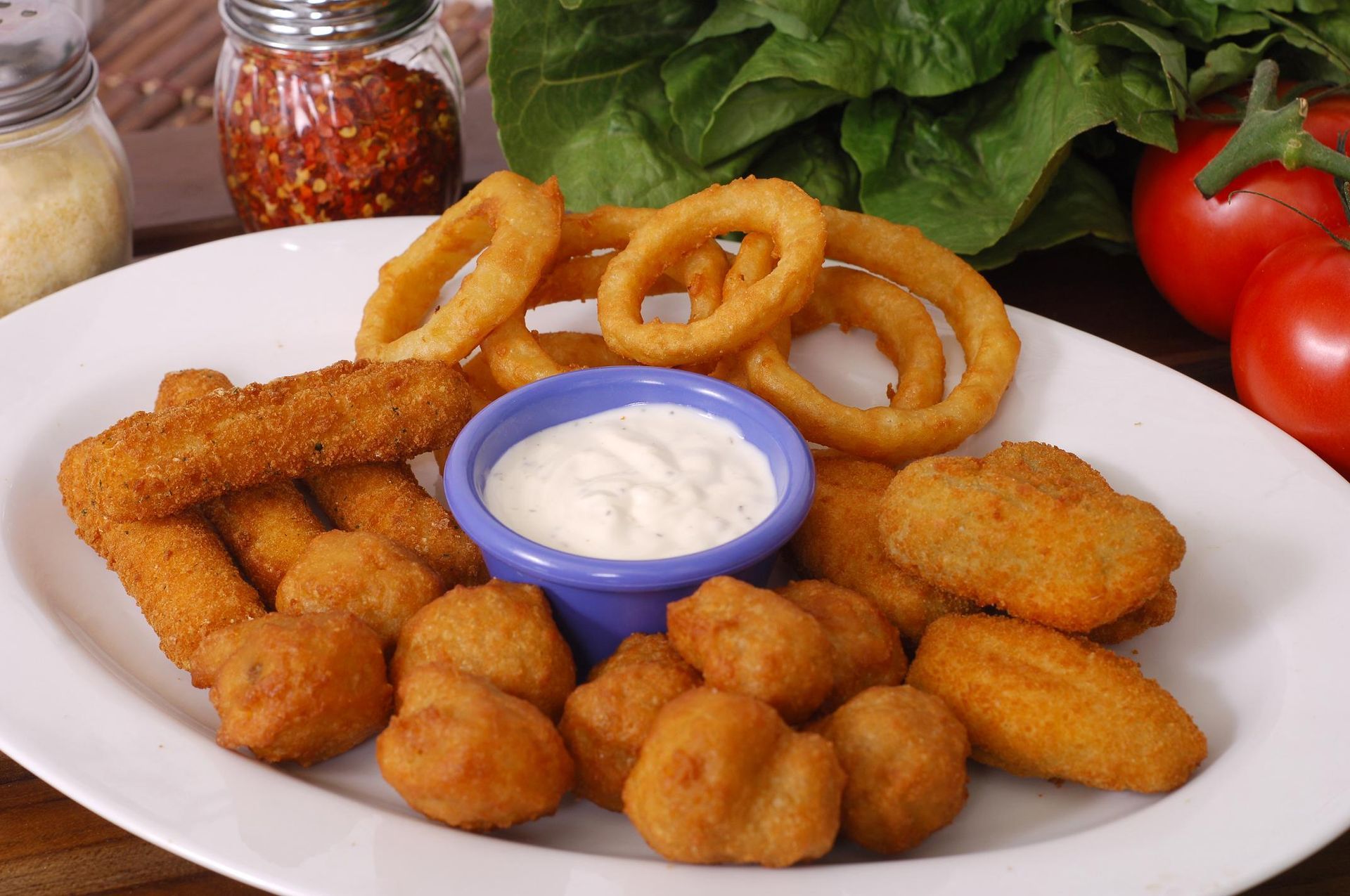 Plate of fried appetizers: onion rings, mozzarella sticks, and mushrooms with dipping sauce.