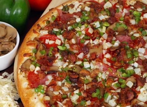 A pizza with a lot of toppings on it is sitting on a wooden cutting board.