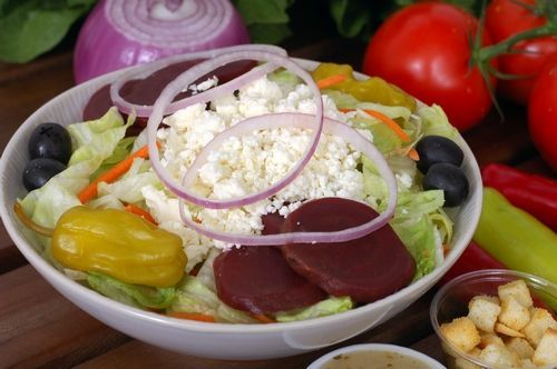 A salad with lettuce, onions, beets, olives, and croutons in a bowl on a table.