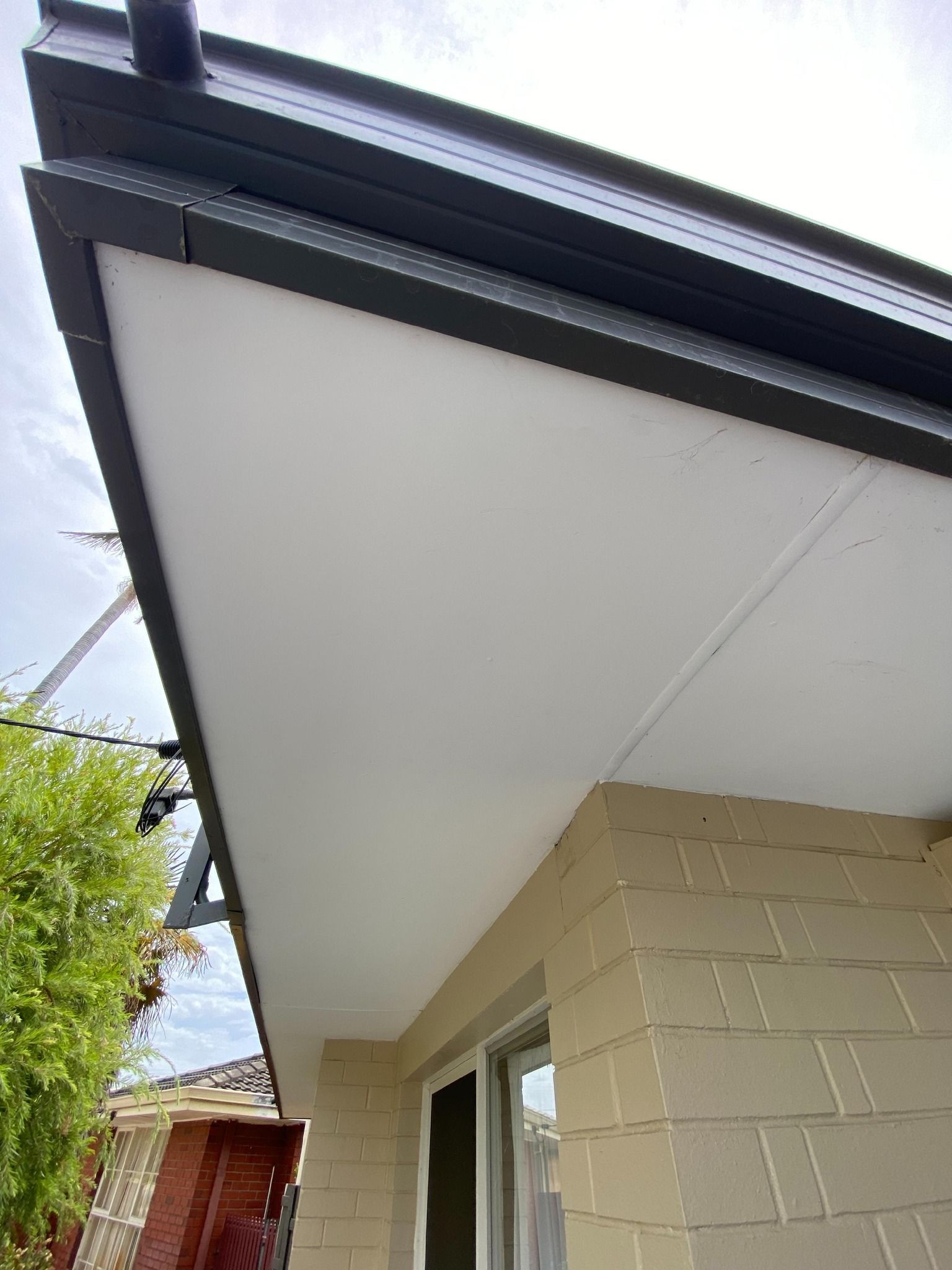 White soffit and dark gutter on a building's exterior, with a brick wall and window visible.