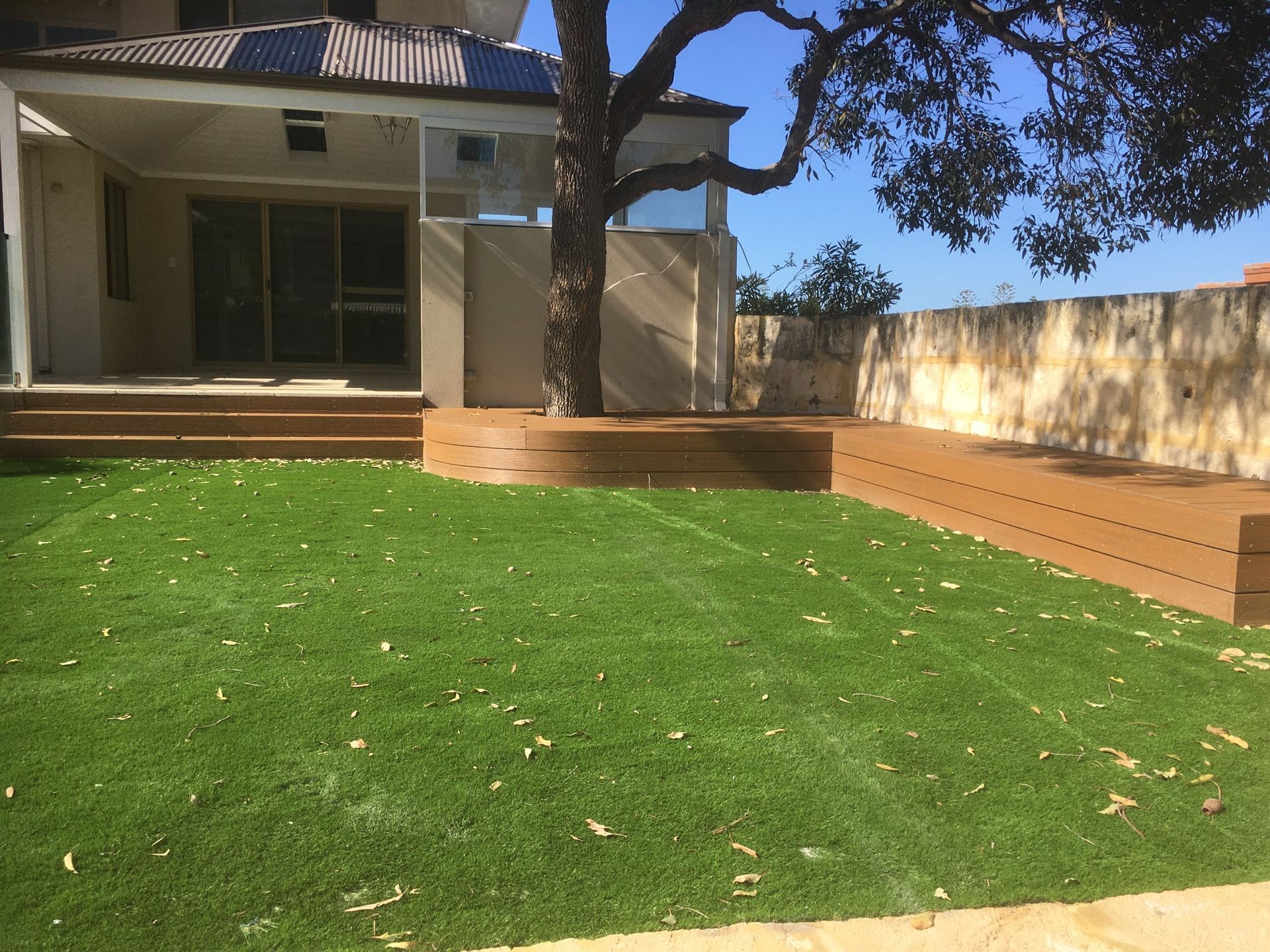 A small tree surrounded by a wooden planter box, on green grass in front of a building.