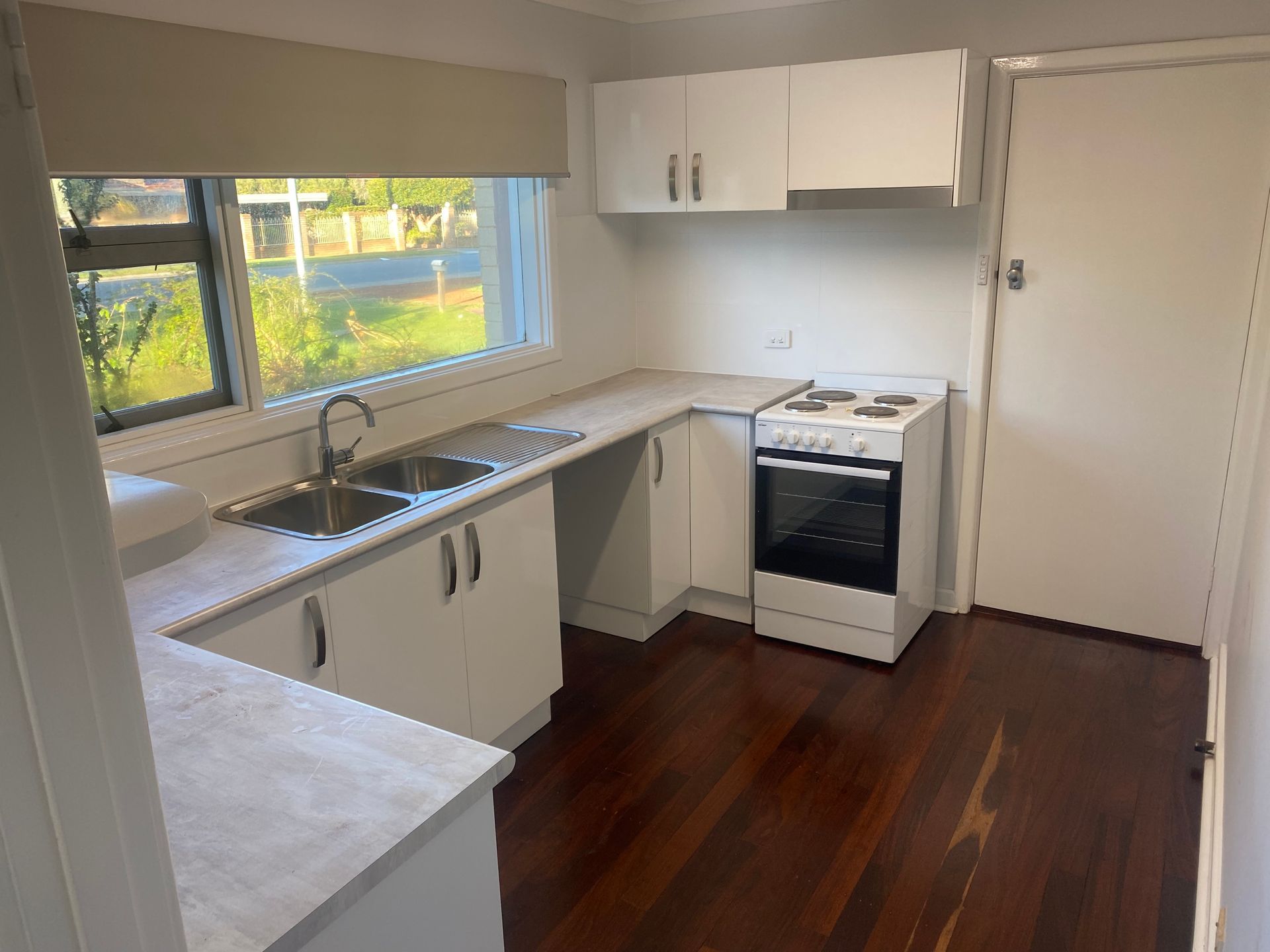 A kitchen with white cabinets , a stove , a sink and a window.