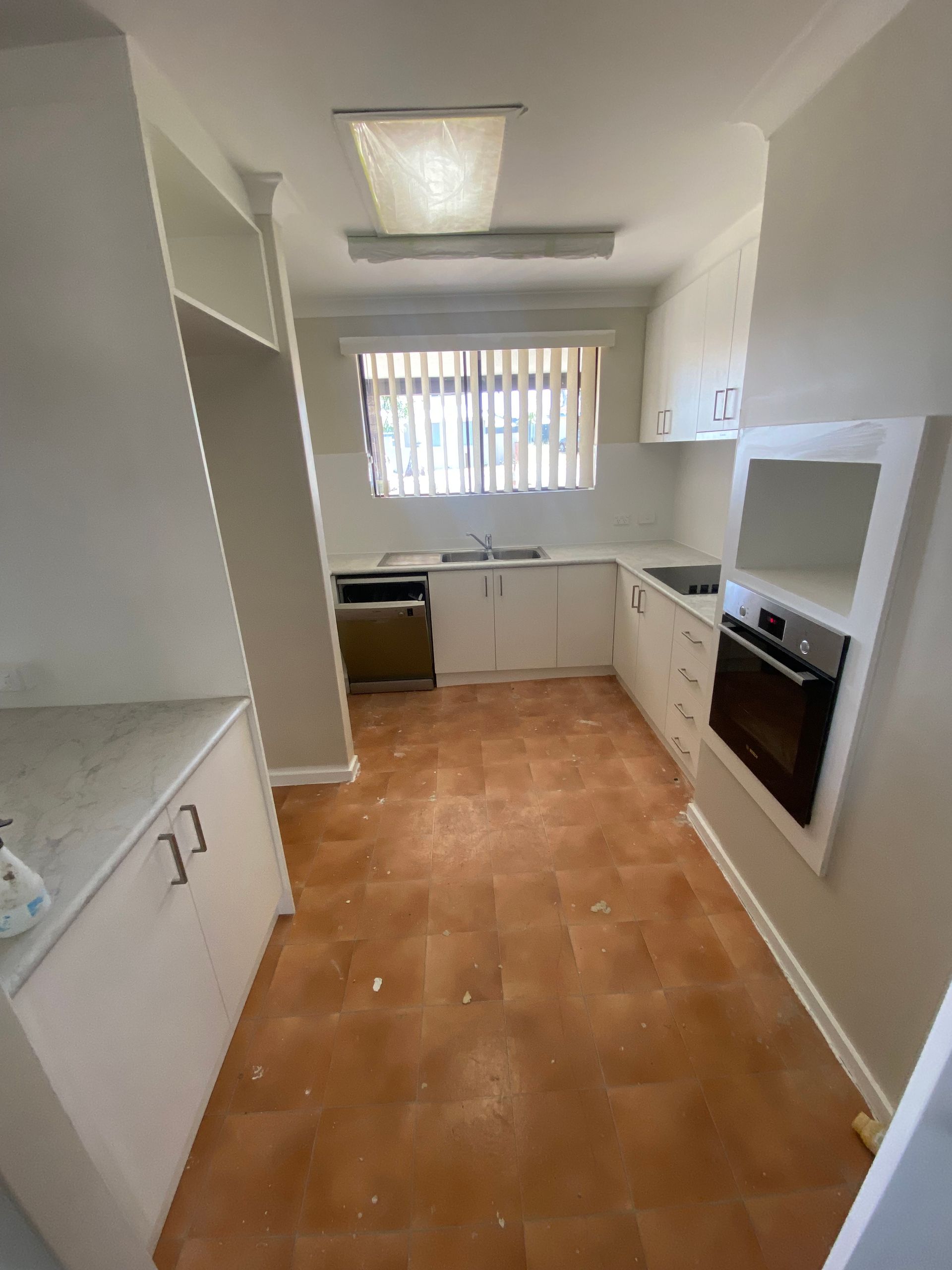 An empty kitchen with white cabinets and a window.