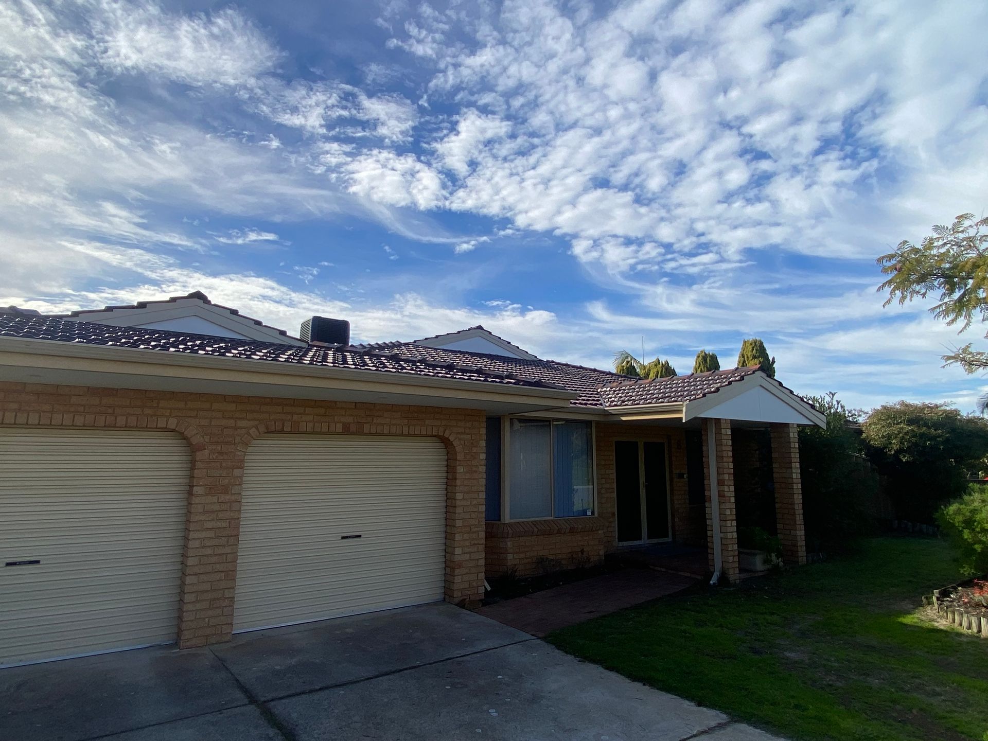 A brick house with two garage doors and a blue sky in the background.