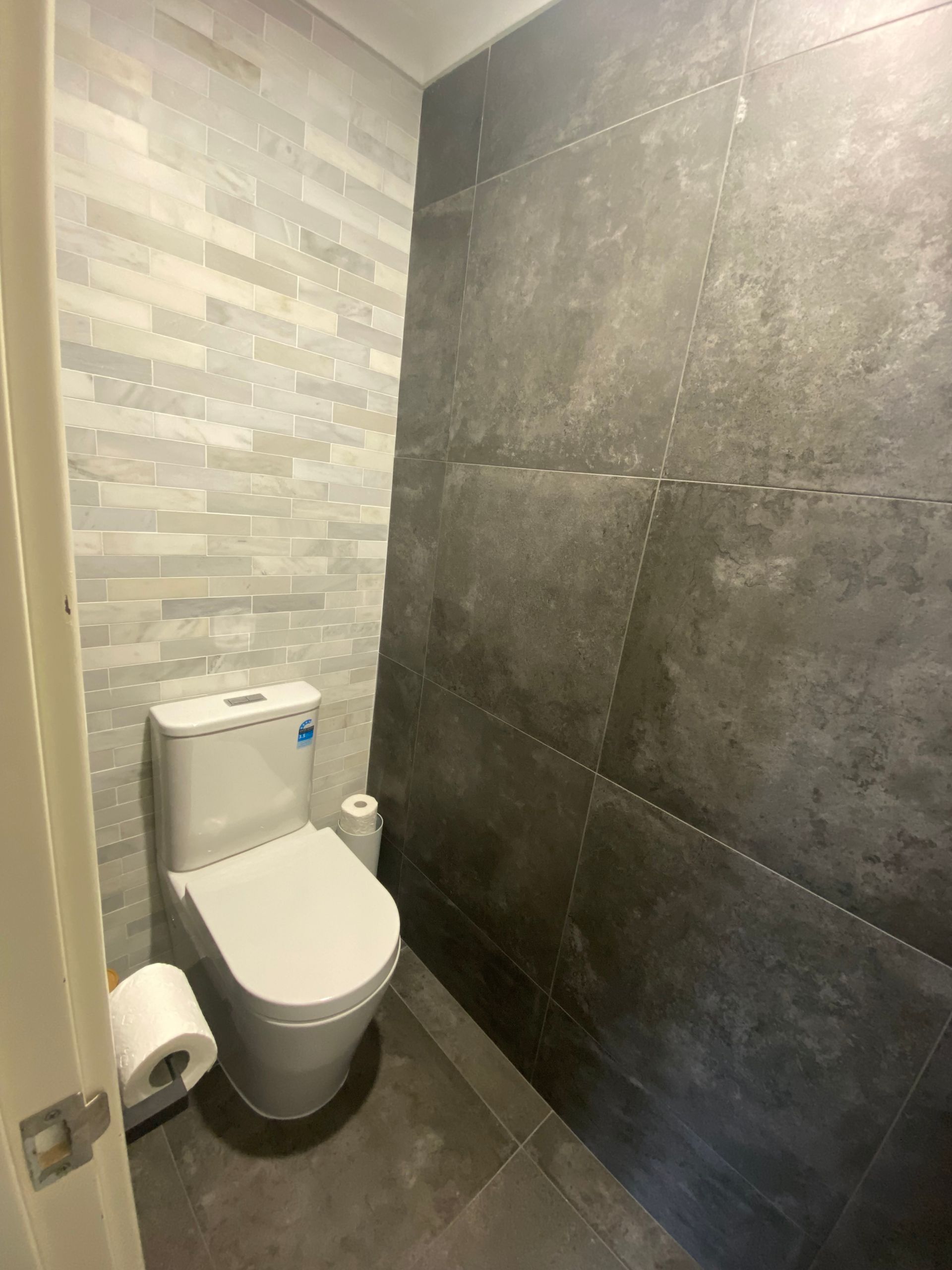 Small modern bathroom with a toilet. Grey and white tiled walls.