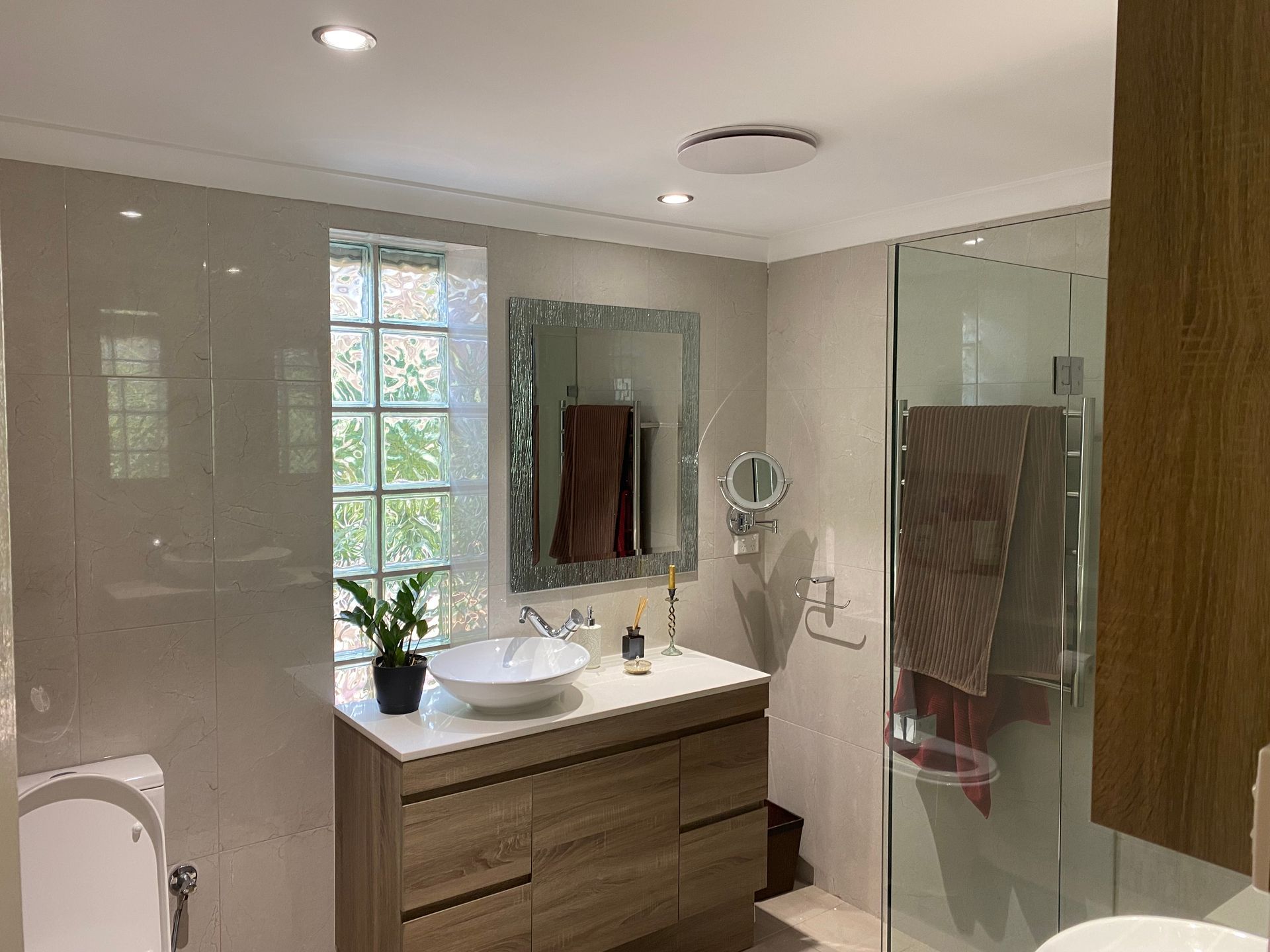 Bathroom with a wooden vanity, a window, and a glass shower door.